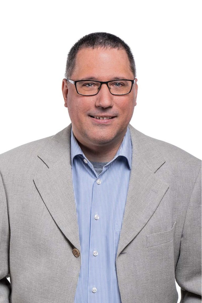 Martin Rӧsler, Leiter des Innenvertriebs, trägt einen hellgrauen Blazer und ein blau gestreiftes Hemd sowie eine Brille und lächelt vor einem schlichten weißen Hintergrund. Professioneller und freundlicher Ton.